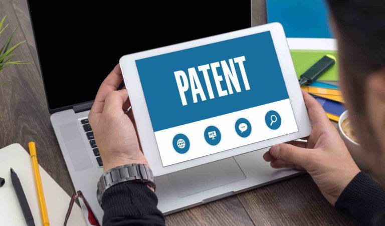 Tabletscreen zeigt das Wort Patent gehalten von einem Mann am Schreibtisch