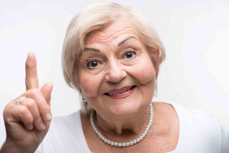 Ältere Dame zeigt mit Zeigefinger auf.