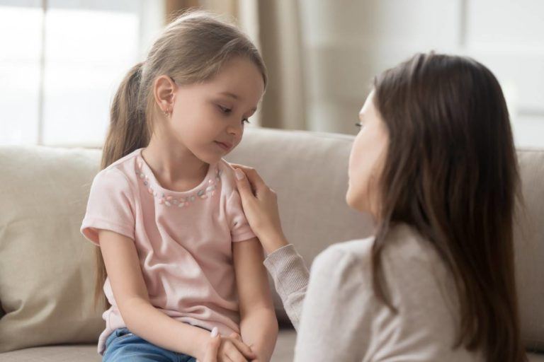 Kind sitzt auf Couch und wird von Mutter getröstet